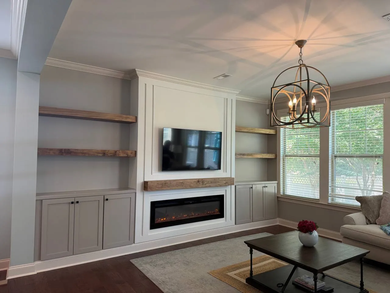 Built-in cabinets with floating wood shelves on both sides of a TV and fireplace wall