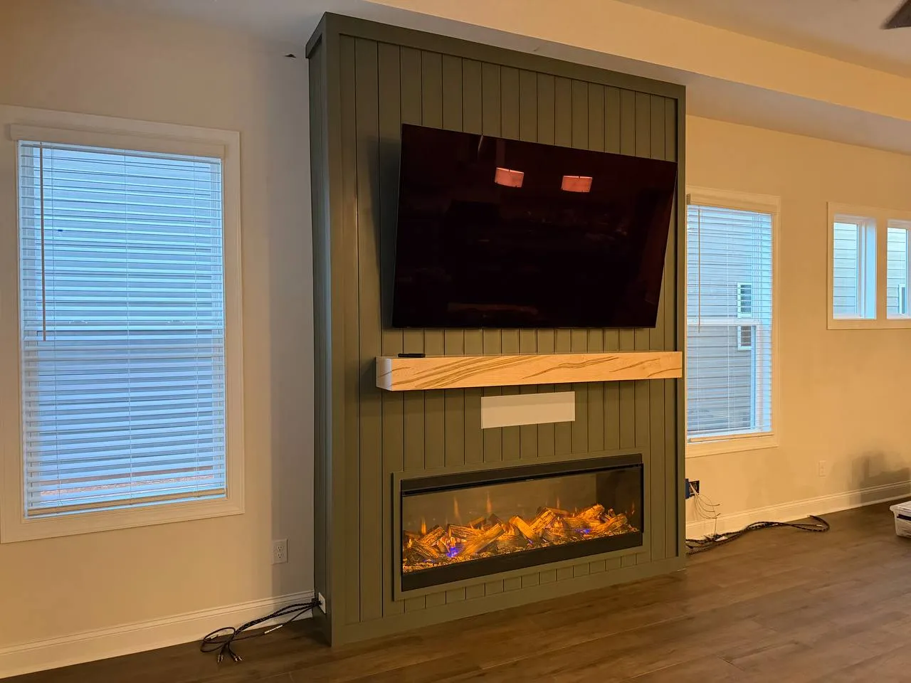 Green vertical shiplap media wall with an electric fireplace, wood mantel and TV